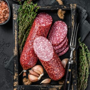 Sliced Dry salami sausage with fresh thyme. Black background. Top view